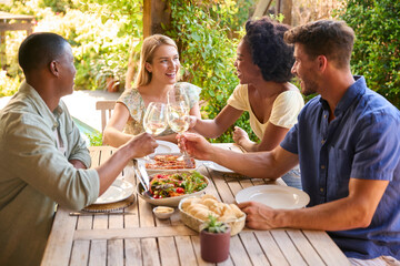 Group Of Smiling Multi-Cultural Friends Outdoors At Home Eating Meal And Drinking Wine Together