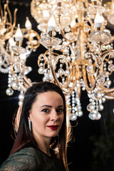 Brunette in a dark dress on the background of a chandelier