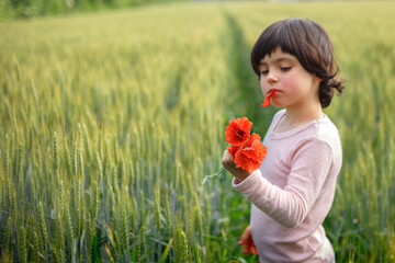 girl with dark hair in pink top holding red poppies in wheat field