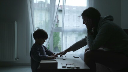 Silhouette of mother and child playing board game at home by window. Childhood education lifestyle. indoors home