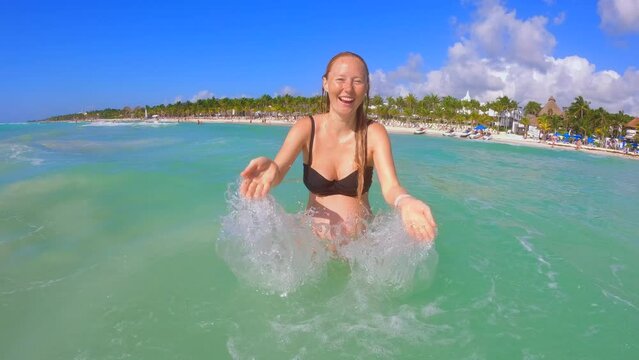 A slowmotion video of a pregnant woman which is having fun in the tropical sea. She is splashing water on the camera.