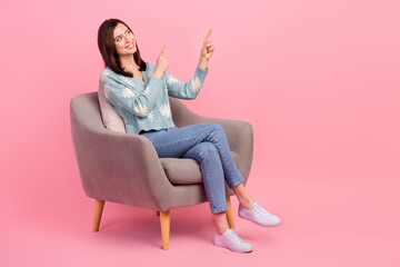 Fototapeta na wymiar Full body cadre of young satisfied woman sitting grey chair recommend point fingers look empty space isolated on pink color background