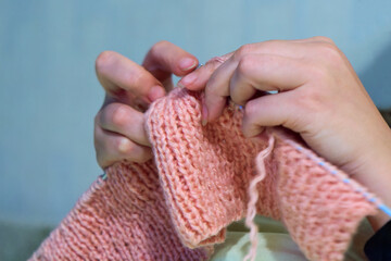 Knitting with knitting needles. The sight of a woman's hands knitting a pink scarf. Close-up