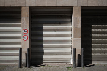 Front view of entrance of the building's service area and shutter doors of garages under typical design of modern building in Europe with cream granite stone facade.