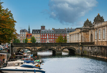 Naklejka premium Copenhagen, Denmark - September 14, 2010: Marmorbroen, historic bridge over canal leading to Christiansborg Slot under blue cloudscape. Colored facades in back, small boats and green foliage