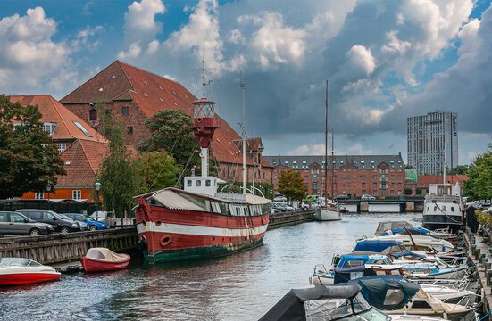 Copenhagen, Denmark - September 14, 2010: Historic red-white lighthouse boat docked in Frederiksholms Canal. Office and residential buildings around. Small boats and blue cloudscape