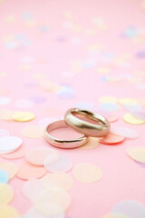 Wedding rings on pink pastel background with paper confetti and copy space focus on rings