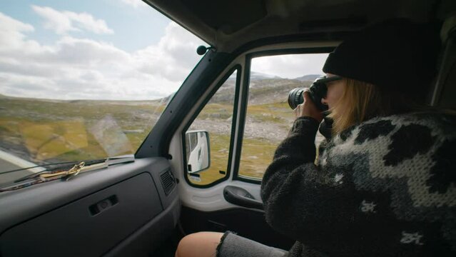 Tourist traveller in cosy sweater make photos on professional camera of epic outdoor landscape during scandinavian road trip. Two friends travel in camper van. Adventure and content creation