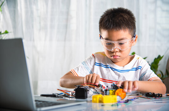 Asian kid boy assembling the Arduino robot car homework project at home, Little child tighten the nut with a screwdriver to assemble car toy, creating electronic AI technology workshop school lesson