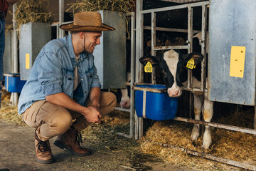 A farmer is crunching next to a cute calf in the stall.