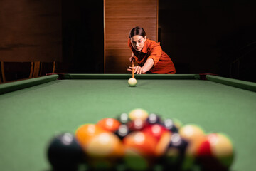 Cute woman with a cue aim at a billiard pyramid of balls, billiards game on. Billiard sports concept
