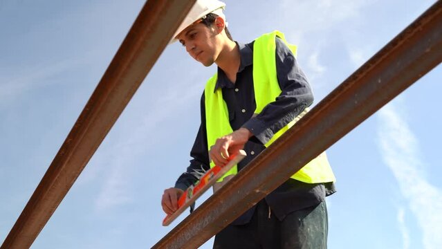Young Arab worker checking the angulation of the beams of the roof of a house with a spirit level. Wearing high visibility vest and white helmet. Concept of construction professionals.