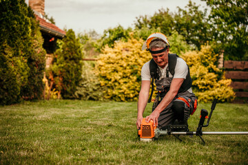 Senior man with a brush cutter on the lawn against the background of bushes in workwear and goggles