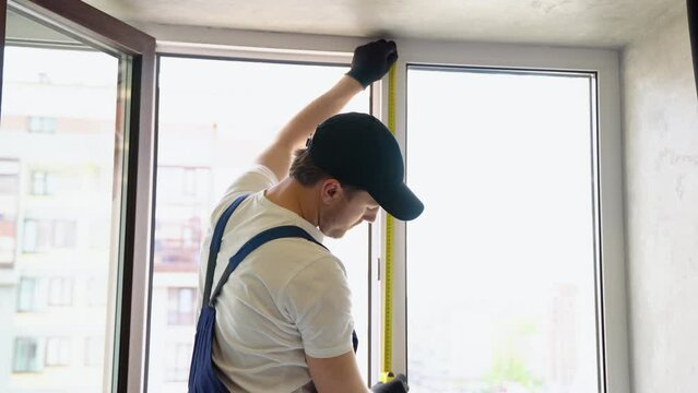Service man in uniform installing pvc window with measure tape in house