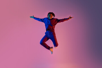Full body length shot of black lady jumping over pink vivid neon light background