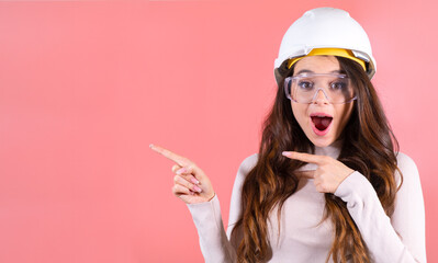 A surprised brunette in a helmet and glasses shows on the copy space on the pink background