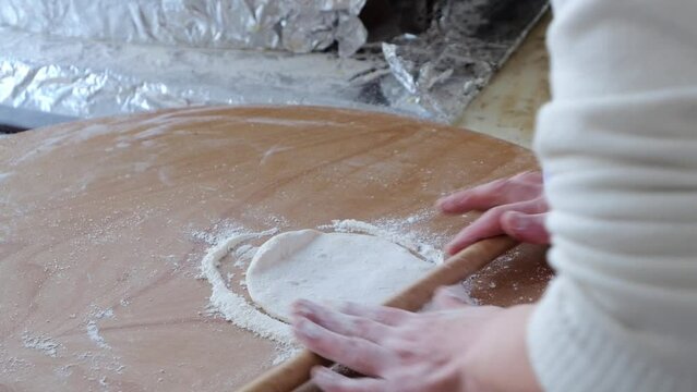 Women's hands roll out the dough on a wooden board, the national dish of Turkey.