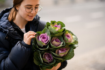 Smiling young woman gently holding beautiful bouquet of ornamental cabbage brassica in hands