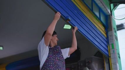 Person opening local storefront garage. Woman sliding up business facade. Entrepreneur of store sidewalk starting the day routine