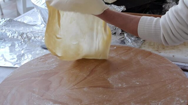 Female hands rotate thin dough on a wooden rolling pin, cooking the national dish of Turkey