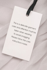 Close up of luxury clothing hang tag. Delicate garment swing tag. Laundry care washing instructions...