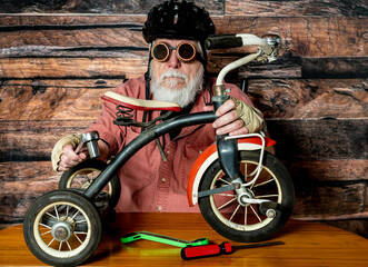 senior male wearing goggles and helmet working on vintage tricycle