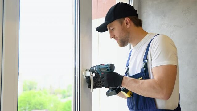 Worker in overalls installing a window lock for home safety. The concept of protecting a child from falling out of windows. Handle with a lock on the window