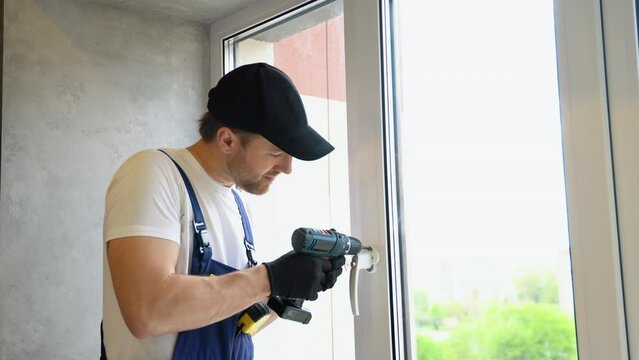 Worker in overalls installing a window lock for hotel room safety. The concept of protecting a child from falling out of windows. Handle with a lock on the window
