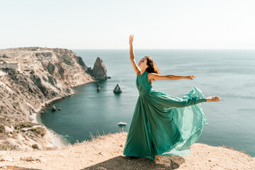 Woman green dress sea. Female dancer posing on a rocky outcrop high above the sea. Girl on the nature on blue sky background. Fashion photo.