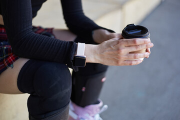 Skater girl sitting in a skatepark with a cup of coffee. Unrecognizable female person wearing inline skates and protective knee pads