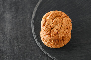 Oatmeal cookies three pieces stacked, on slate stone plate round, dark background, top view, selective focus