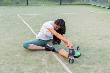 Young woman stretching sitting on floor on padel court with racket	