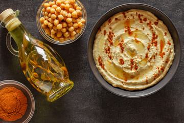 Hummus with olive oil and red pepper in grey bowl, on slate stone plate round, dark background, top view