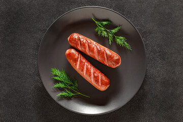 Two grilled sausages and springs of dill on dark background, top view, space to copy text