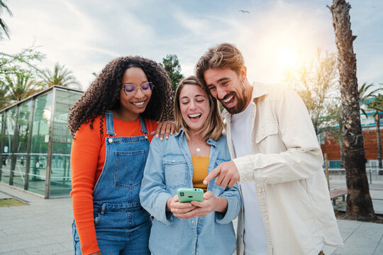 Group of multiracial friends having fun with a mobile phone watching funny videos on social media, play games, send messages. Three young happy people smiling and laughing using a callphone together