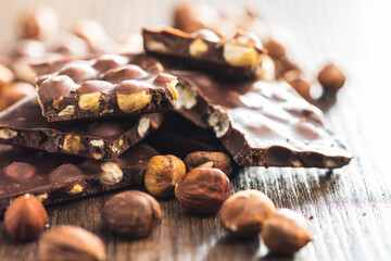 Broken chocolate bars with  nuts on wooden table.