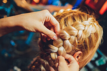 Process of braiding the master weaves braids on her head blond little girl in beauty salon close up. Professional hair care and creating hairstyles. © Евгений Вершинин