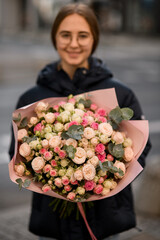 Woman florist holding in hands beautiful bouquet of small gentle roses in wrapping paper