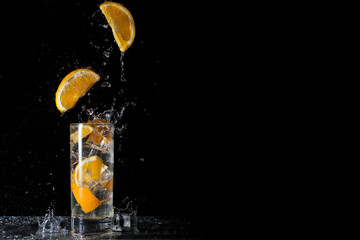 Cool and fresh drink of orange lemonade with orange slices and ice on a black background with falling orange slices and ice
