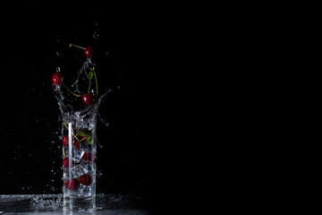 Cold drink from Cherry lemonade and ice on black background with splashes and falling ice
