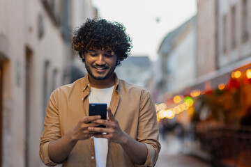 Close-up of a Latin American man walking through the evening city, a man types a message on the phone, calls and browses the Internet online, uses mobile applications