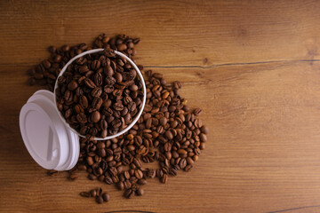 a paper cup of coffee on a wooden table with coffee beans