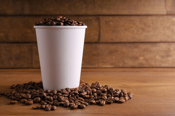 a paper cup of coffee on a wooden table with coffee beans