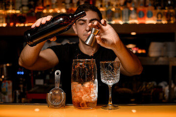 Bar accessories and tools for making cocktail stands on the bar counter and bartender adds an ingredient to cocktail
