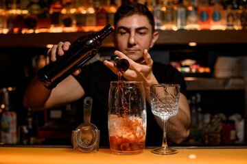 Bar accessories for making cocktail stands on the bar counter and bartender adds an ingredient to cocktail
