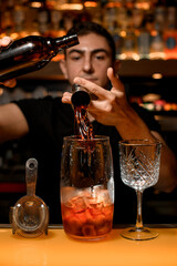 Tools for making cocktail stands on the bar counter and bartender adds an ingredient to cocktail