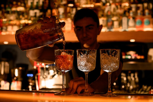 Alcohol pours from measuring glass cup through the strainer to cocktail goblet
