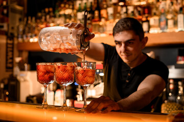 Professional bartender fills cocktail glasses with alcohol using measuring cup and strainer
