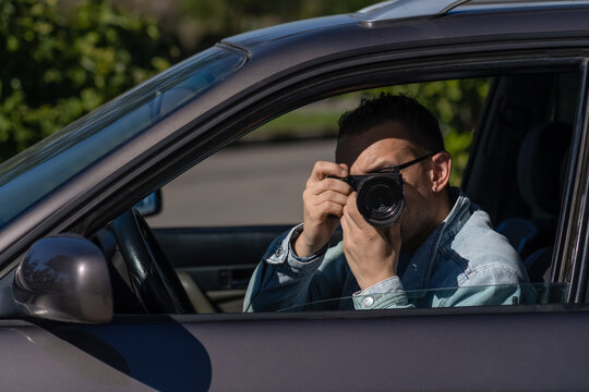 Pivate detective an in sunglasses, sitting in a car and carrying out surveillance, takes pictures with a professional camera