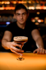 Barman holding glass with cold espresso martini cocktail in pub, closeup.